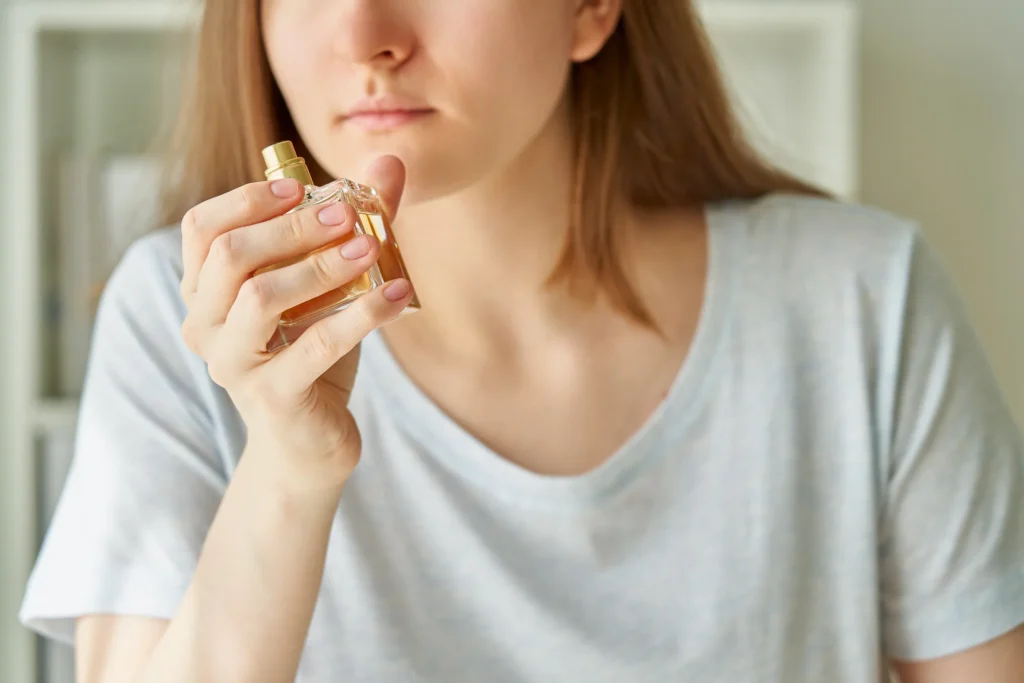 Joven con playera gris oliendo un frasco de perfume Santal 33.