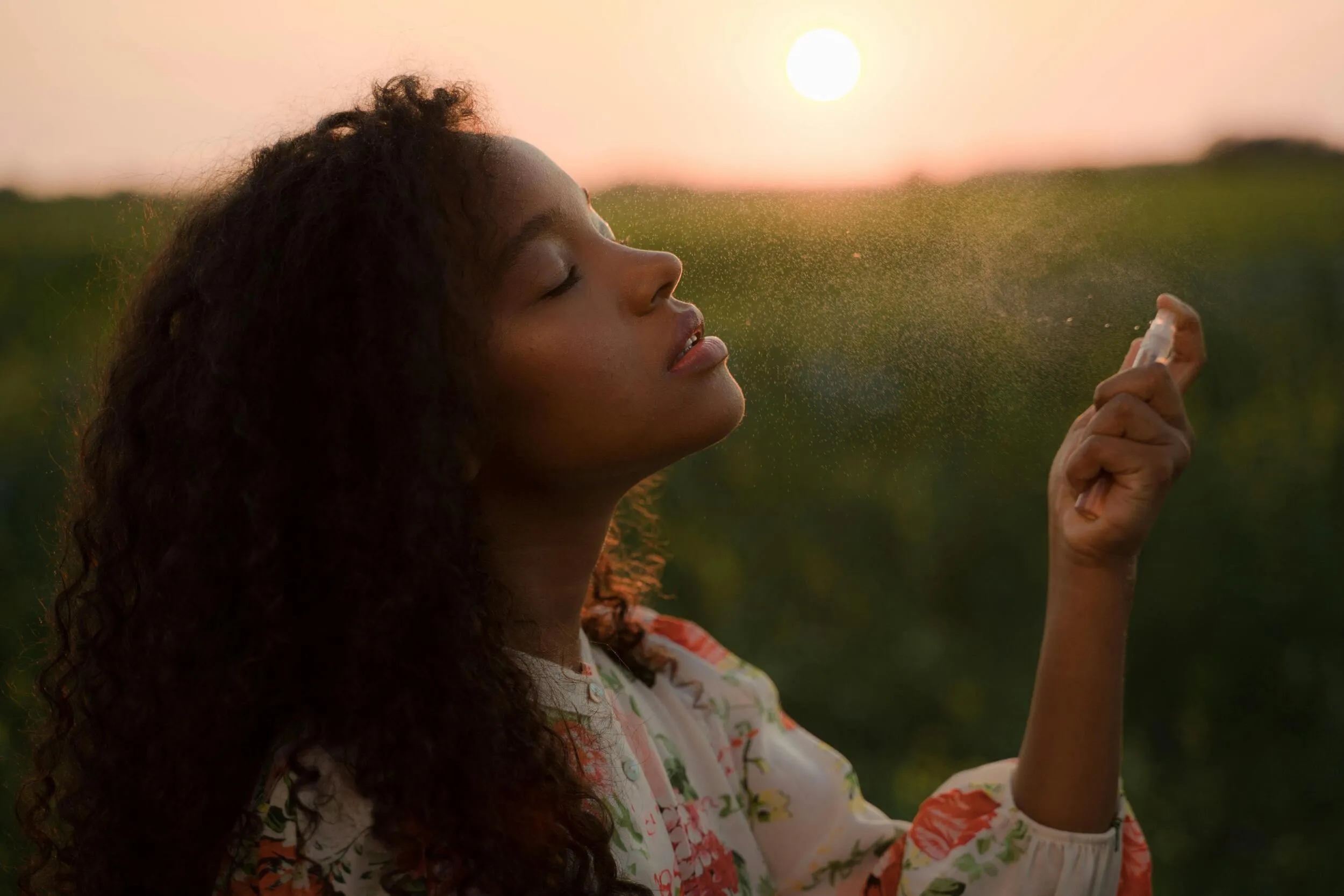 Mujer aplicando perfumes al aire libre mientras disfruta una fragancia fresca al atardecer