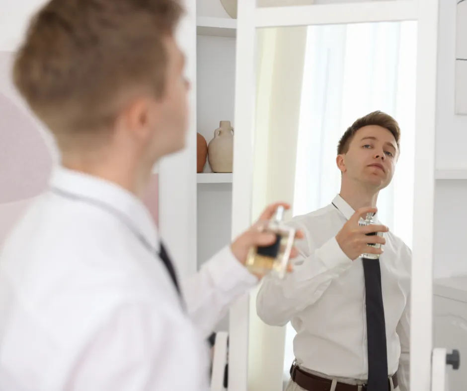 Hombre vestido de manera formal aplicándose perfumes para hombre frente al espejo antes de ir a la oficina